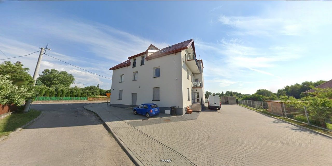 Seitenansicht der Fassade eines Wohngebäudes mit rotem Dach, weißem Putz und Balkonen