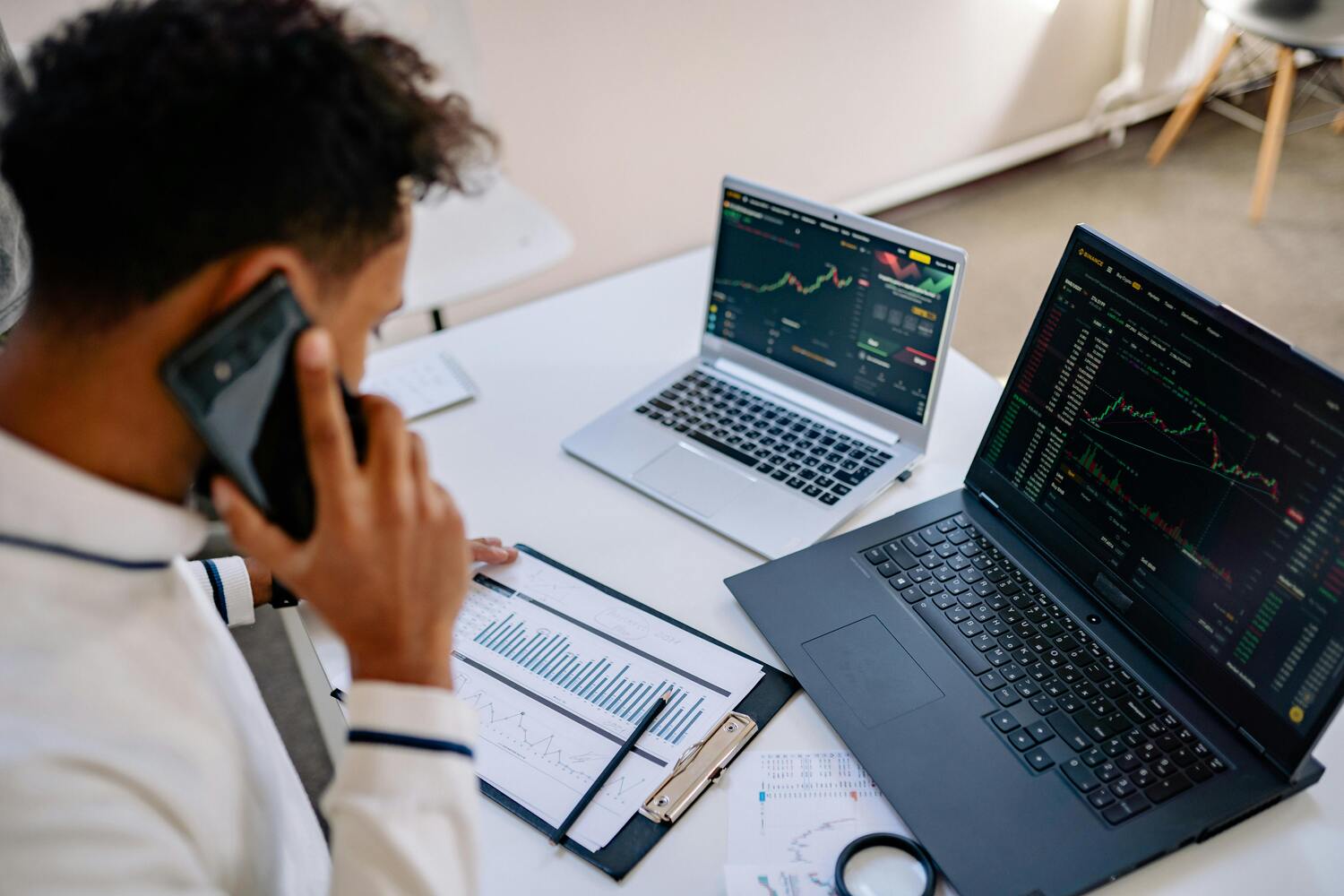 Analyst verfolgt Diagramme auf zwei Laptops und einen Bericht auf einem Klemmbrett – Marketing-Leistungsüberwachung