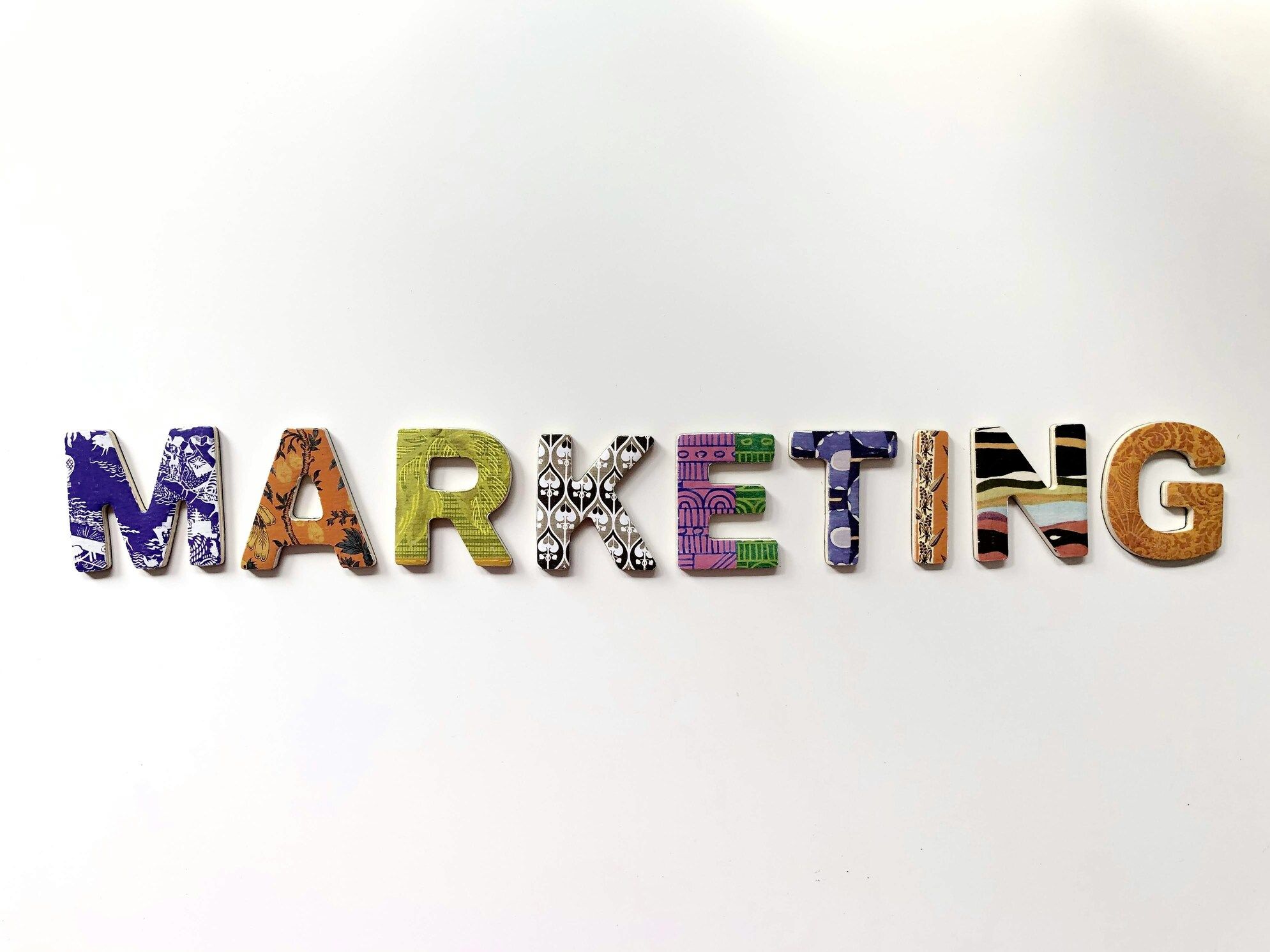 Bunte Holzbuchstaben, die das Wort „MARKETING“ auf weißem Hintergrund bilden